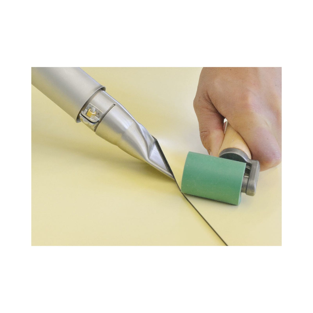 Hand using a tool with a green roller on a light-colored surface